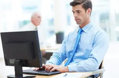 Professional man in blue shirt and tie using computer at desk.