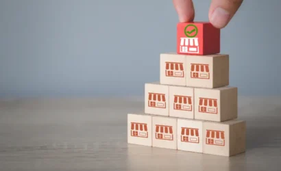 A person carefully adds a red block onto a stack of wooden blocks, creating a stable tower.