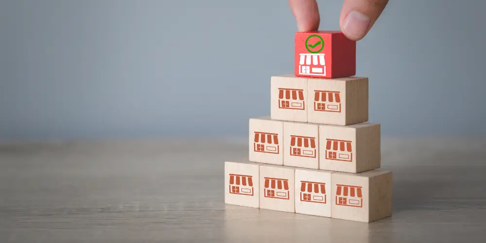 A person carefully adds a red block onto a stack of wooden blocks, creating a stable tower.