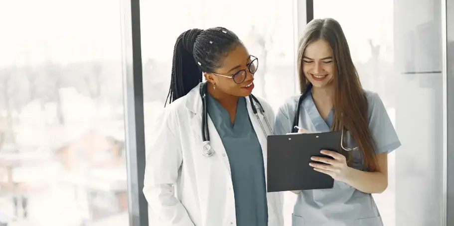 Two women in medical attire analyzing data on a tablet screen.