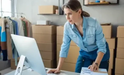 Woman typing on computer surrounded by boxes in room.